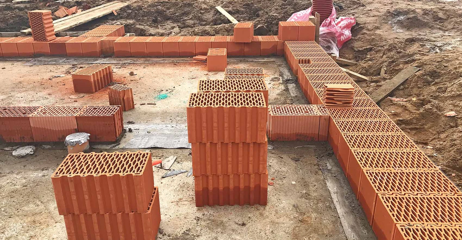 Процесс строительства: рабочий укладывает первый ряд крупноформатных керамических блоков на слой гидроизоляции поверх фундамента